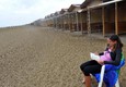 Una donna legge un libro accanto a una fila di capanne deserte sulla spiaggia del Lido di Venezia a  causa del maltempo © Ansa