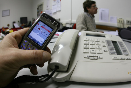 Una persona  tiene in mano un cellulare vicino a un telefono di rete fissa. Foto d'archivio ANSA / FRANCO SILVI © ANSA 